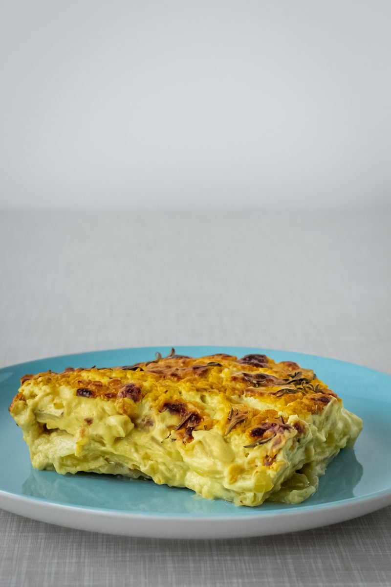 A piece of the best creamy and vegan dauphinoise potatoes, served on a turquoise plate.