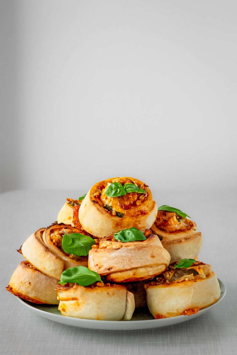 Vegane Pizzaschnecken, mit Basilikum dekoriert, auf einem Teller gestapelt