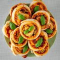 vegan pizza rolls, filled with vegetables and vegan cheese, topped with fresh basil, placed on a pastell green plate.
