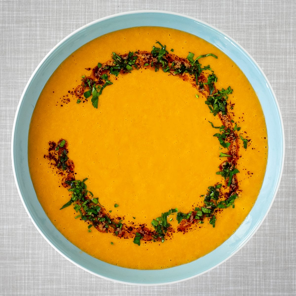 A turquoise plate filled with a creamy red lentil soup, on a grey vintage kitchen table