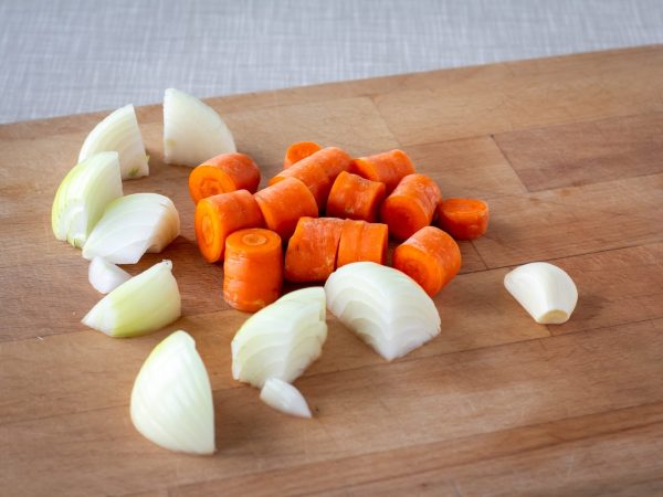 Carrots and onion on a cutting board, already cut into chunks, ready for a red lentil soup.