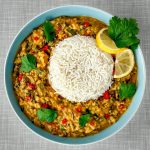 A turquoise plate featuring a creamy Swiss chard and lentil curry served with basmati rice, garnished with cilantro leaves, a twisted slice of lemon, and chili rings. Photographed from above.