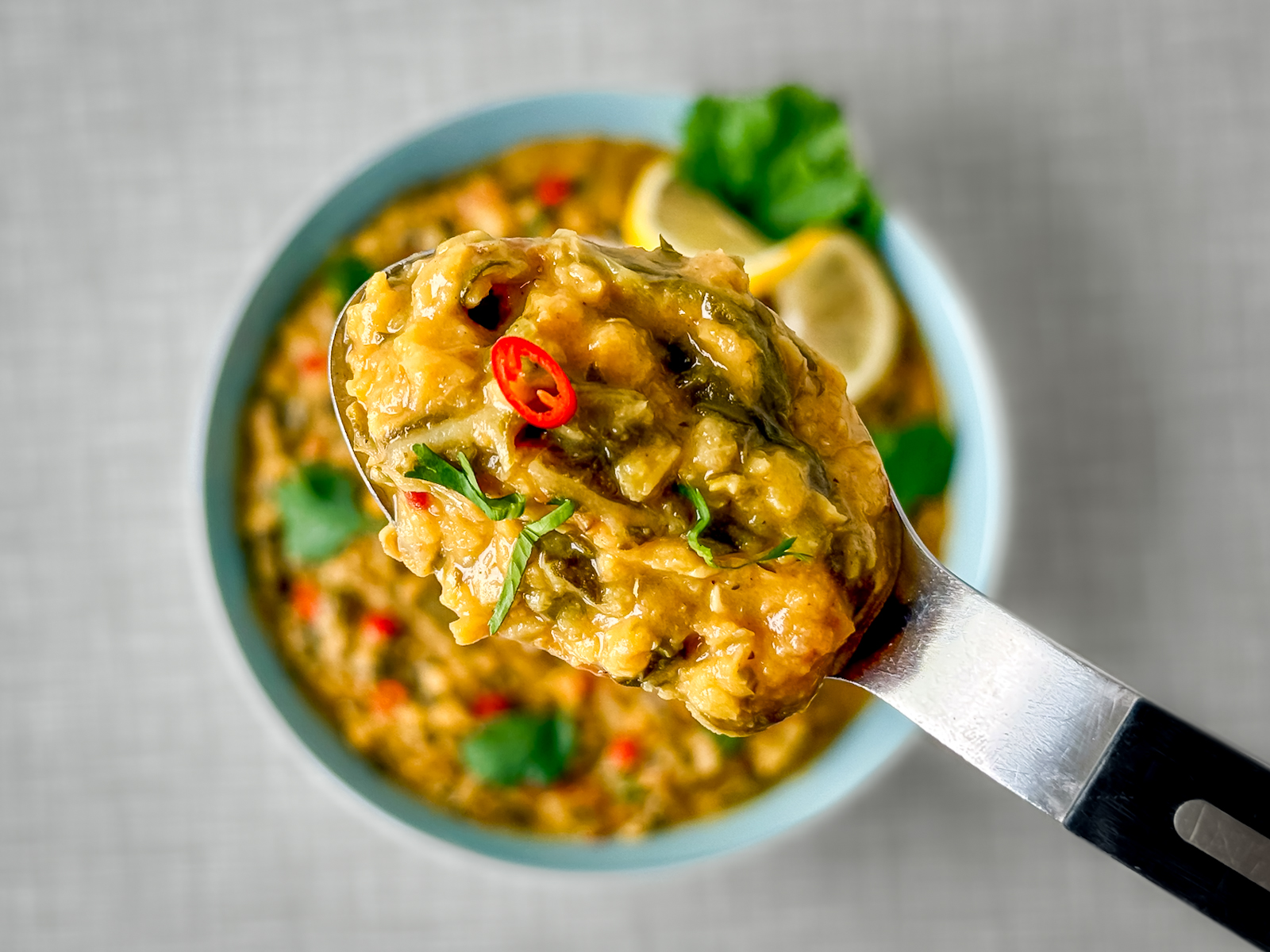Close-up of a spoonful of Swiss chard and lentil curry, with the plate in the background.