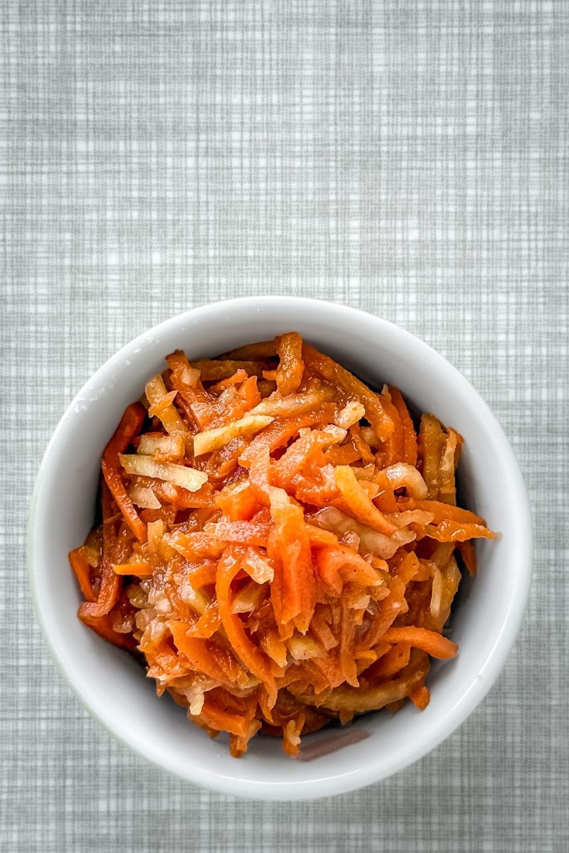 Eine Portion Karotten-Kimchi in einer kleinen Schüssel auf einem grauen Tisch, von oben fotografiert.