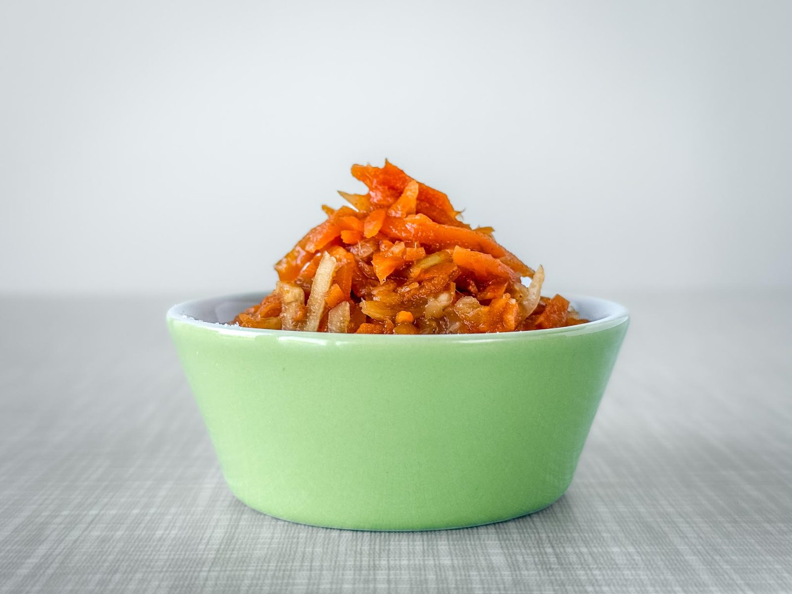 Eine kleine pastellgrüne Schüssel, gefüllt mit Karotten-Kohlrabi-Kimchi.