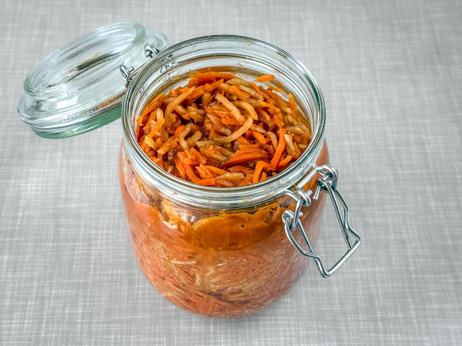 Ein geöffnetes Bügelverschluss-Glas, gefüllt mit Karotten Kohlrabi Radieschen-Kimchi