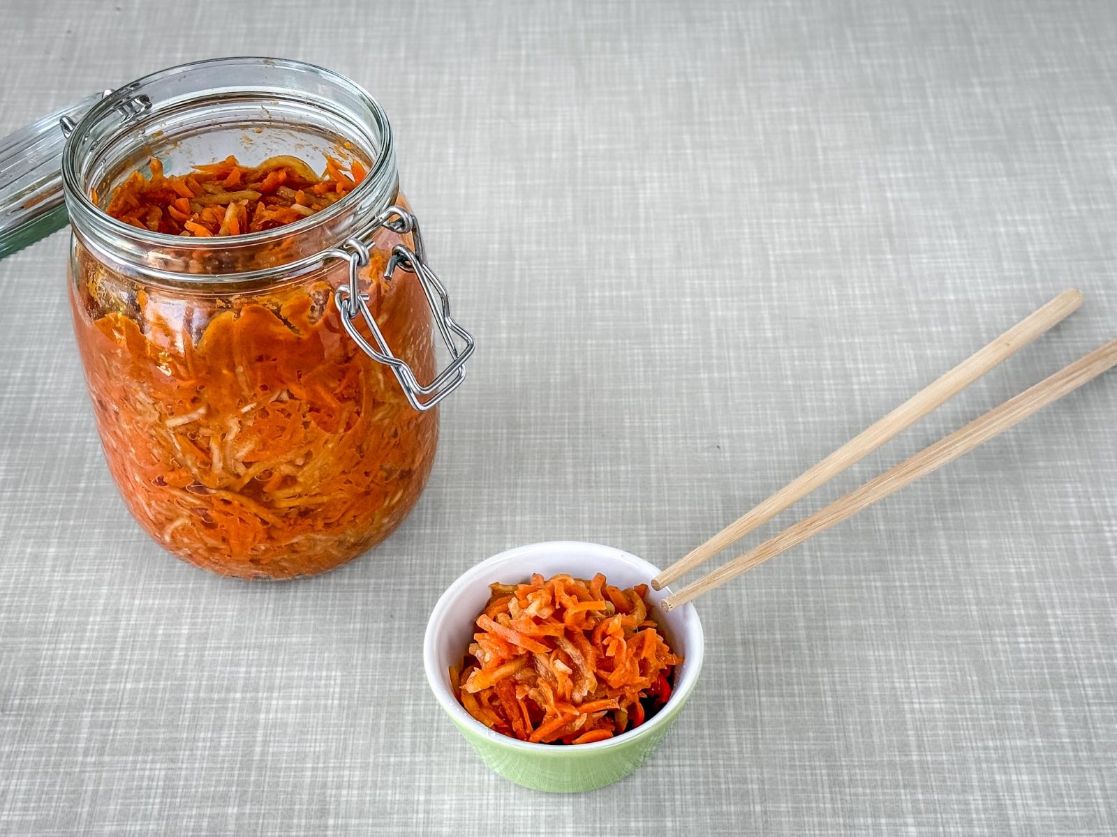 Ein geöffnetes Bügelverschluss-Glas, gefüllt mit Karotten Kohlrabi Radieschen-Kimchi. Daneben eine kleine Schüssel, gefüllt mit Kimchi.