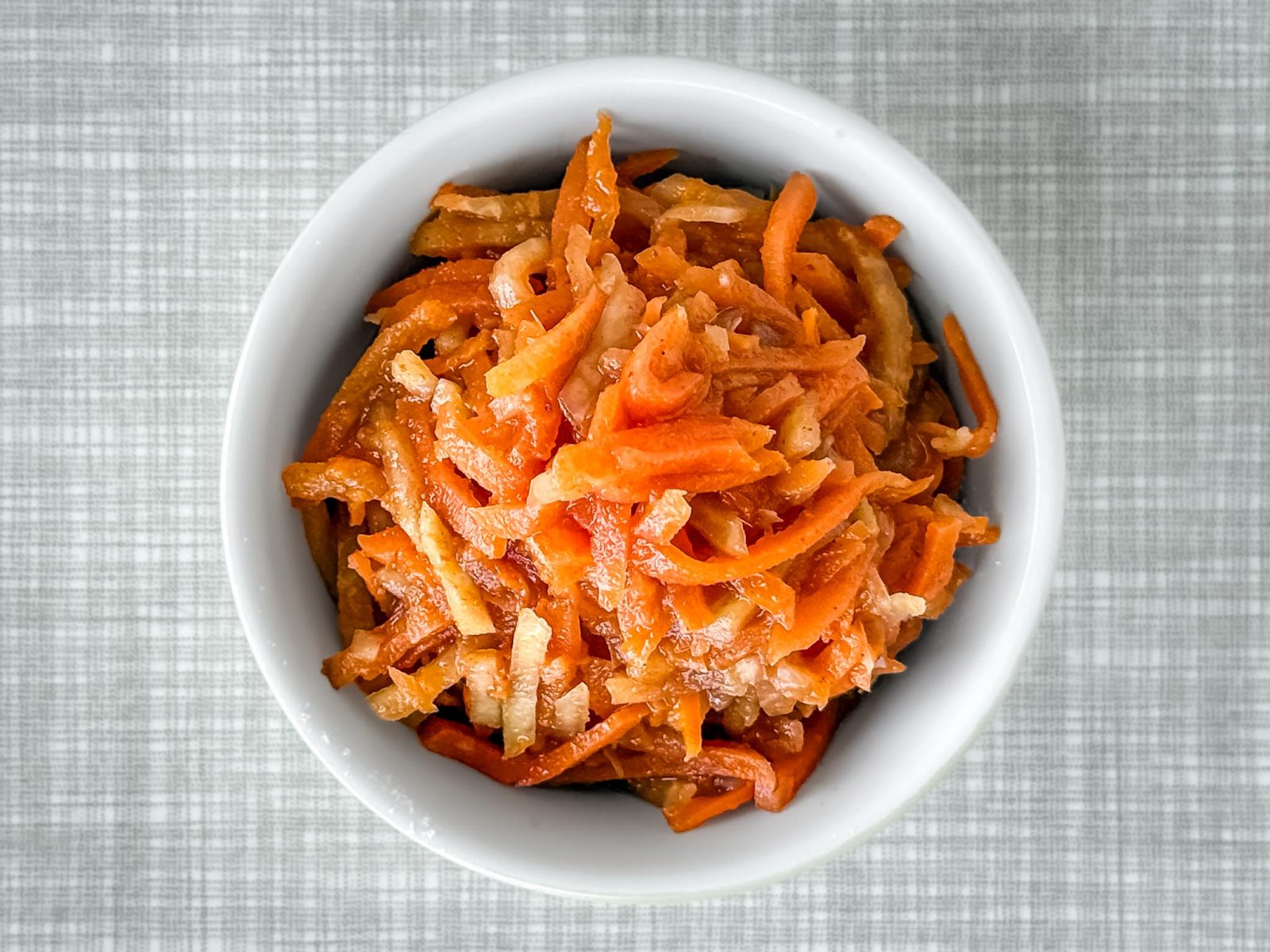 Eine kleine Schüssel, gefüllt mit einem Karotten Kohlrabi Radieschen-Kimchi, von oben fotografiert.