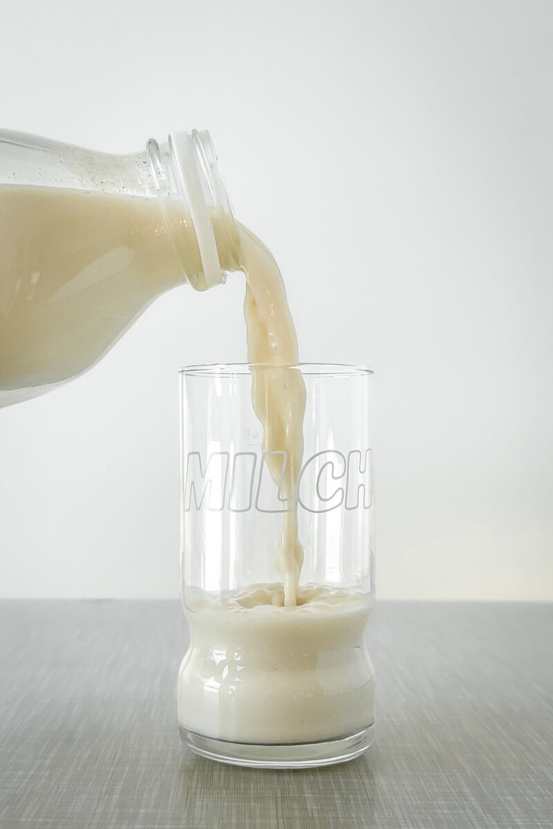 Homemade oat milk is poured into a glass. 1970s vintage milk glass