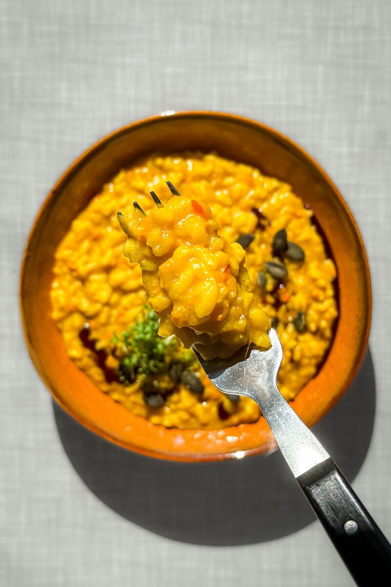 Eine Gabel mit Kürbisrisotto, im Hintergrund der Teller mit dem Risotto, von oben fotografiert.