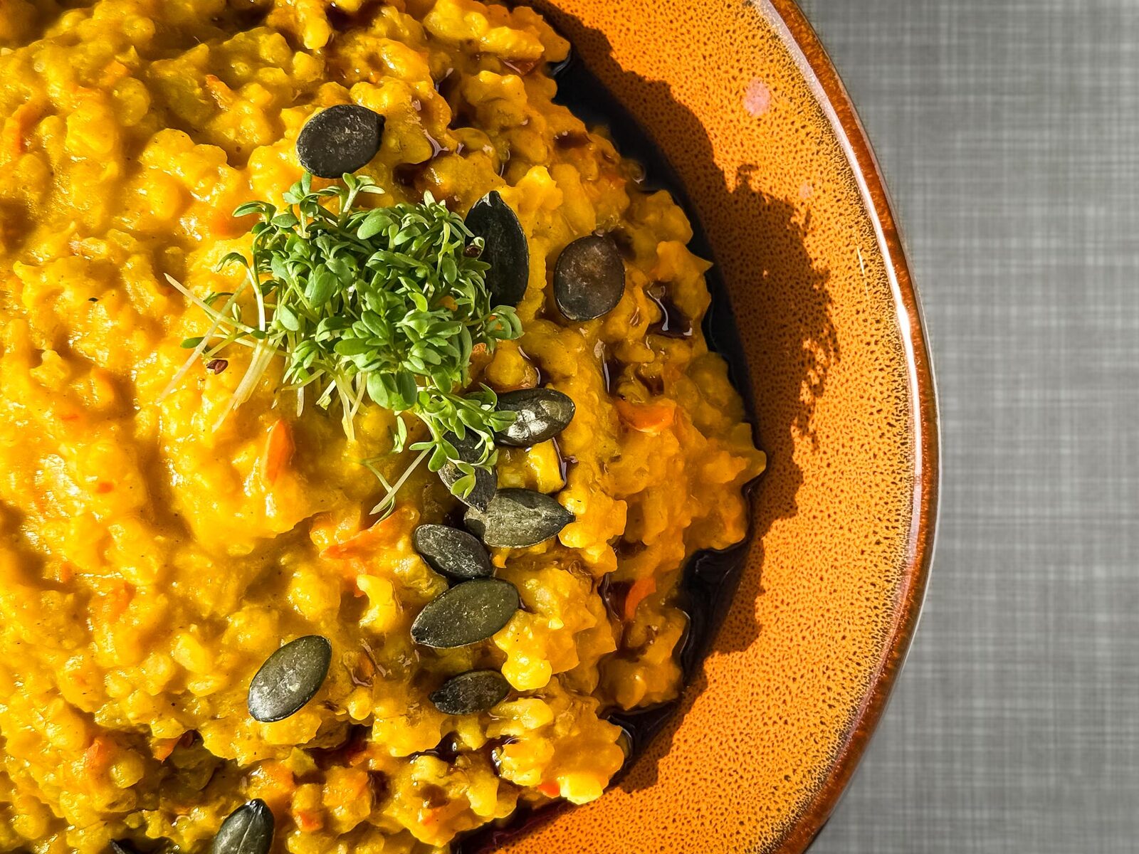Cremiges Kürbisrisotto mit Kürbiskernöl, Kürbiskernen und Kresse verfeinert, Nahaufnahme von oben.