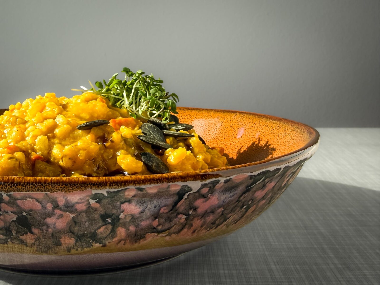 Cremiges Kürbisrisotto mit Kürbiskernöl, Kürbiskernen und Kresse verfeinert, Ausschnitt, Nahaufnahme von schräg vorne fotografiert.
