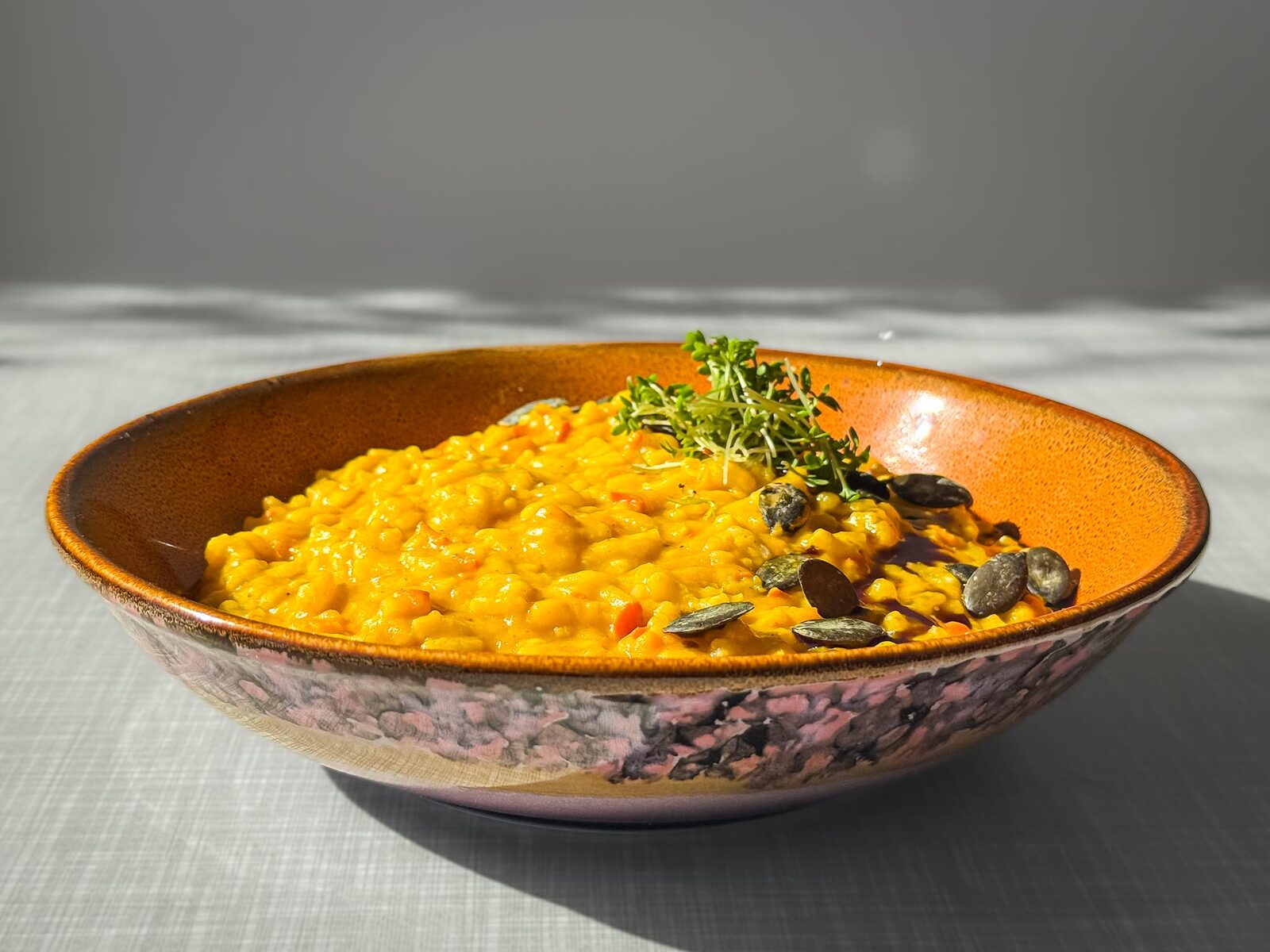 Cremiges Kürbisrisotto mit Kürbiskernöl, Kürbiskernen und Kresse verfeinert, von schräg vorne fotografiert.